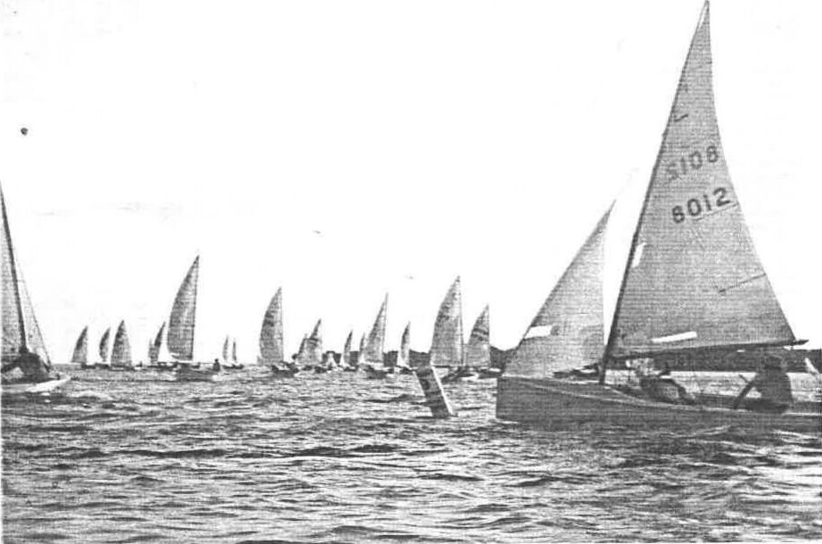 A fleet of Albacores racing on choppy water, sail number 8012 in the foreground
