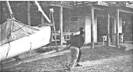 A sailor hauling on a line beside a rigged Albacore in a boat shed
