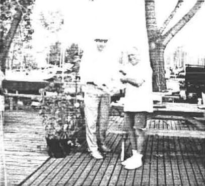 Ian Aukema presenting the participation trophy to George Roth on a wooden deck under a tree