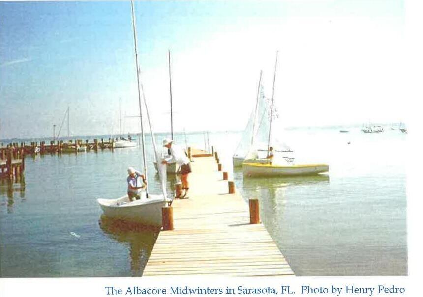Sailors rigging Albacores at a dock in Sarasota, Florida, with a loaded dinghy dock and open water beyond