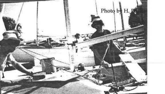 Two sailors rigging an Albacore at a Sarasota dock, dinghy park in the background