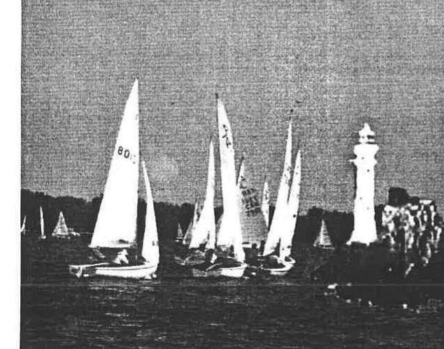 A fleet of Albacores sailing past a lighthouse