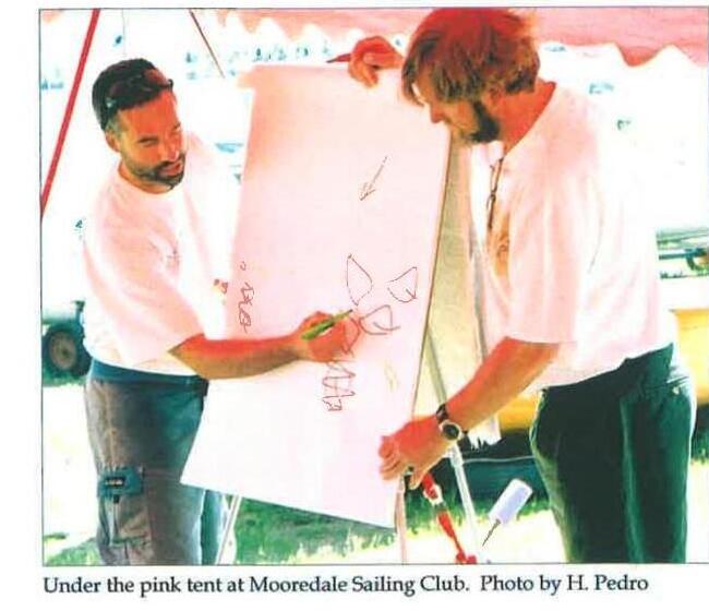 Two men marking up a whiteboard under a pink tent at Mooredale Sailing Club