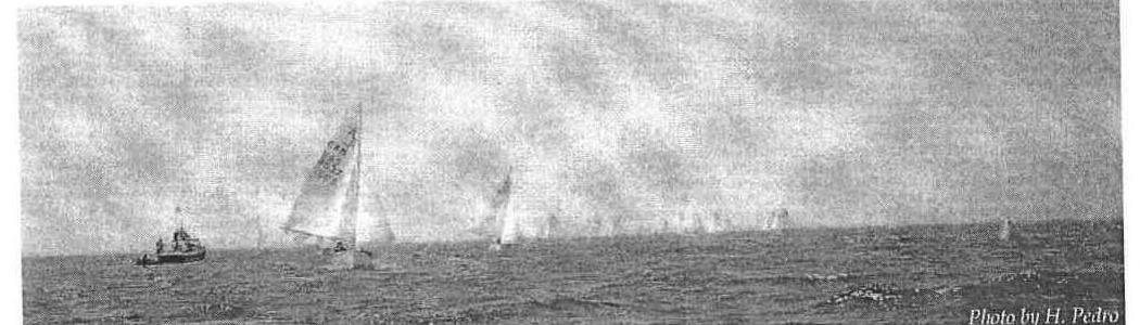 A fleet of Albacores racing in hazy conditions off Toronto, with a committee boat in the foreground. Photo by H. Pedro