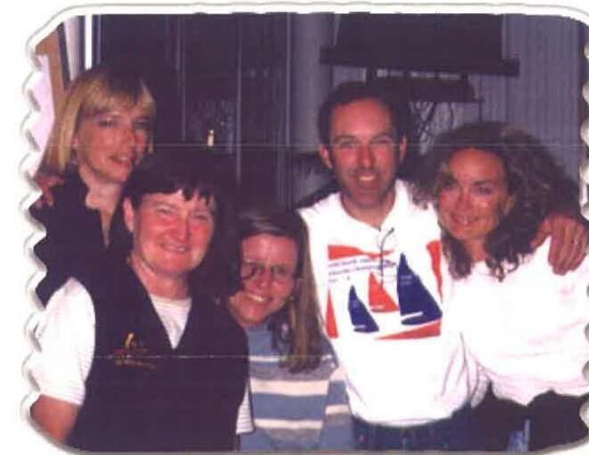 Five sailors smiling and embracing indoors at an “Aprés Sailing” gathering