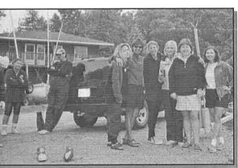 A group of seven sailors posing together beside a truck and trailer in a clubhouse parking lot