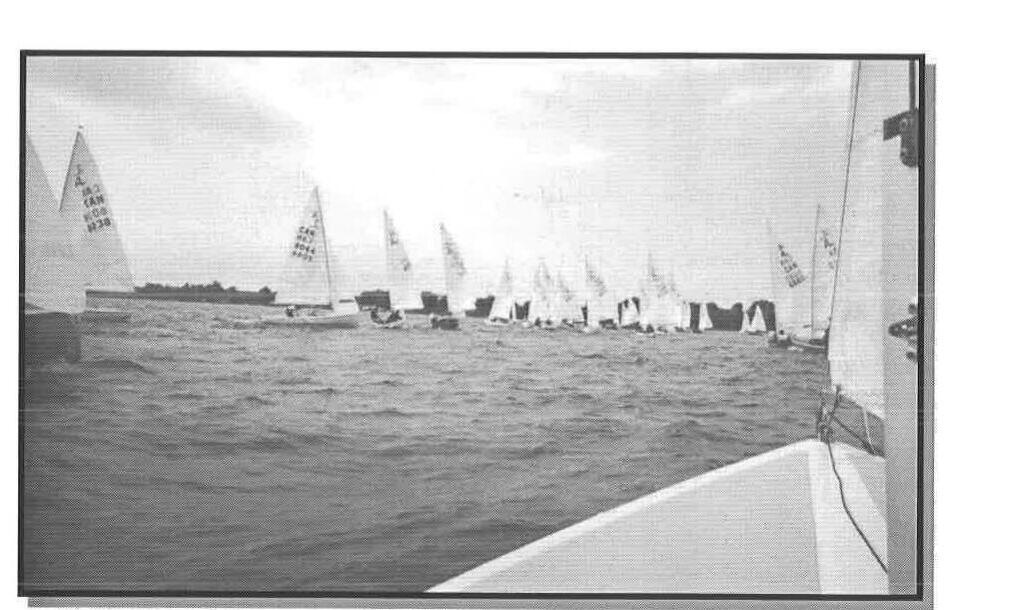 A fleet of Albacores at a start line, viewed from the bow of a committee or chase boat