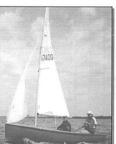 A single Albacore under full sail with two crew aboard on flat water