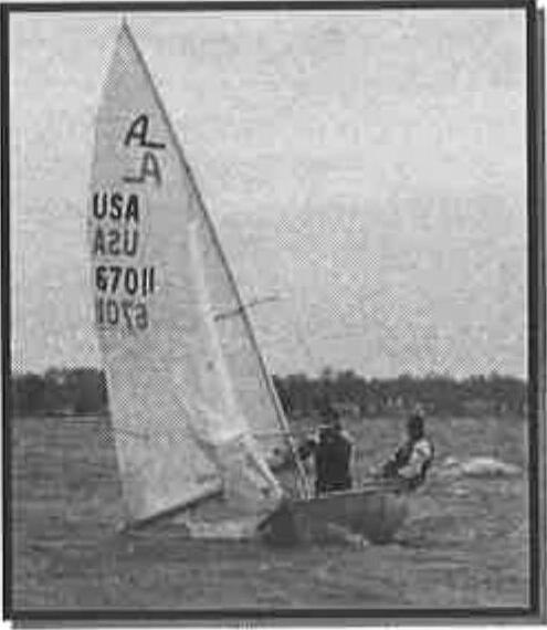 An Albacore heeled over in high wind with two crew forward, jib luffing