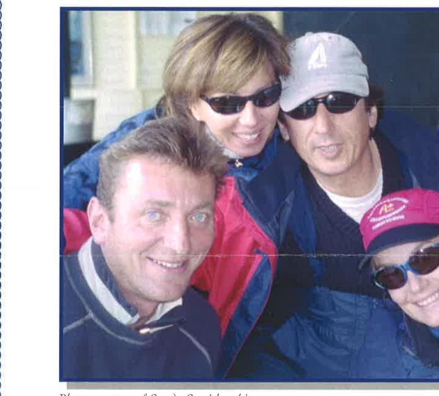Four sailors bundled in jackets and sunglasses posing closely together after racing