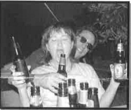 Two sailors clinking beer bottles together at a nighttime gathering, surrounded by empty bottles