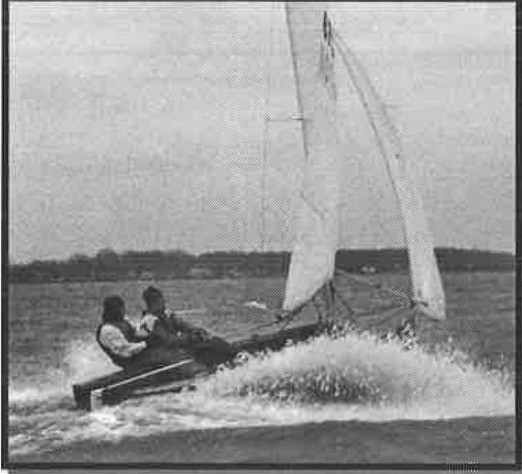 An Albacore powering downwind at speed with spray flying off the bow, two crew hiked aft