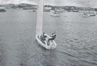 Two sailors aboard an Albacore in a harbor, seen from above