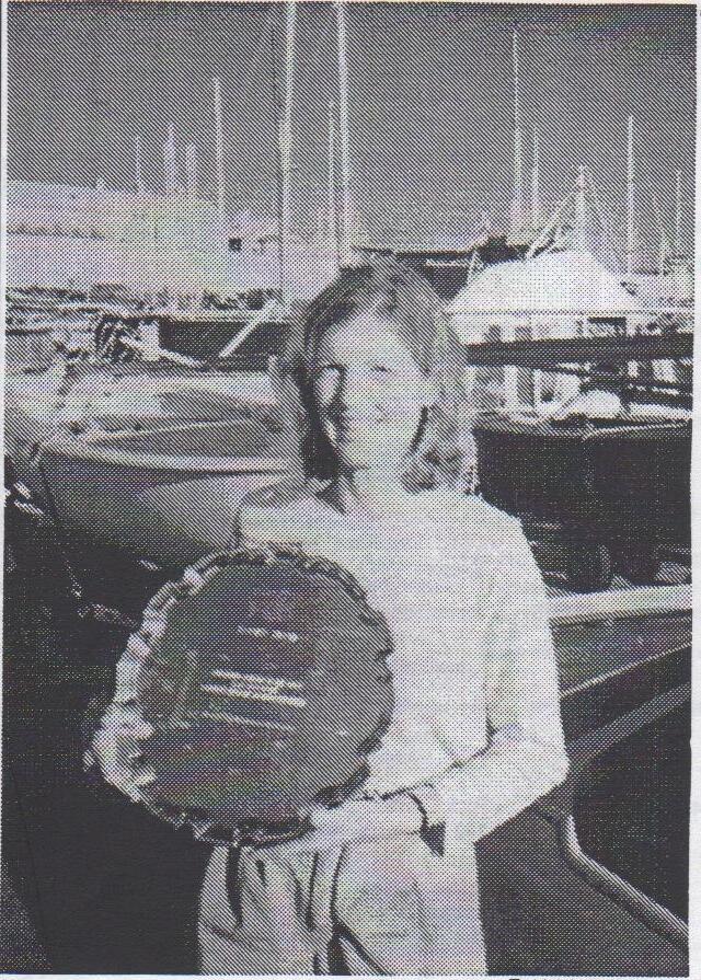 Ann White standing on a dock in front of moored boats, holding a large round trophy plate
